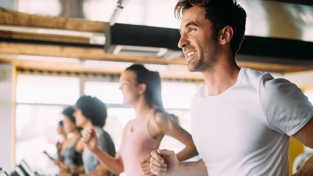 Man running on a treadmill with other exercisers in the background.